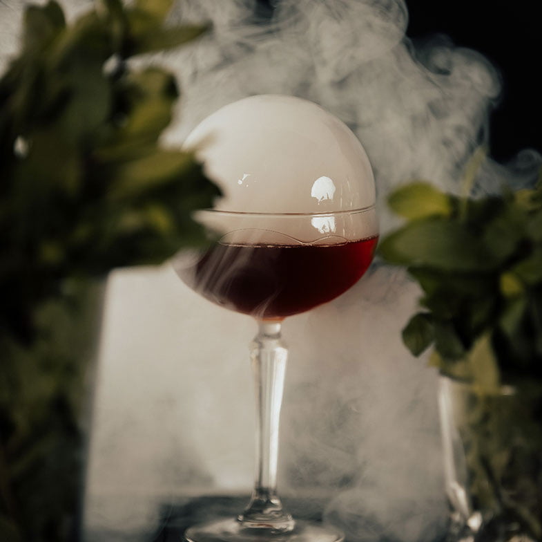 Cocktail servido en copa de cristal con burbuja de humo encima y humo alrededor