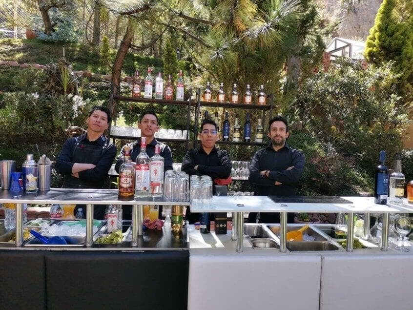 Cuatro bartenders posando detras de una barra grande negra y blanca en un jadín en evento corporativo en Bolivia