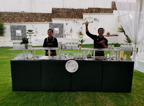 Dos bartenders detras una barra negra grande en un jardín