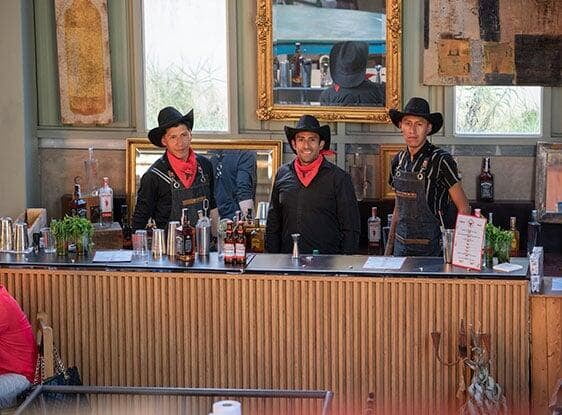 Tres bartenders en un barra grande de madera en evento temático de vaqueros